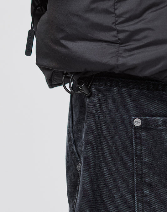 Close-up of a person wearing dark denim jeans and the LIVE FAST DIE YOUNG Live Fast Puffer Jacket in an oversized fit, featuring a drawstring with plastic toggle near the waistband and large visible front pocket.