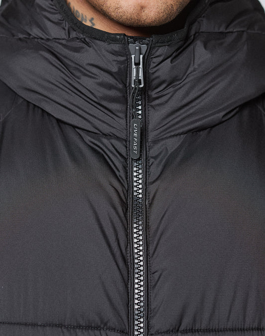 Close-up of the Live Fast Puffer Jacket by LIVE FAST DIE YOUNG, shown zipped up with a pull tag labeled LIVE FAST. The image also captures part of the wearer's neck and a partial tattoo.