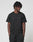 A person with short, twisted hair stands against a white background, wearing the LIVE FAST DIE YOUNG Basic Chest Tee in black and matching cotton shorts, hands in pockets and looking slightly to the side.