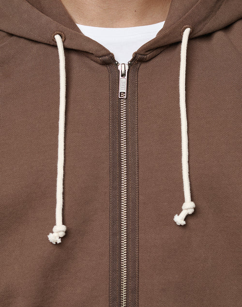 Close-up of the LFDY Lightweight Hooded Zip by LIVE FAST DIE YOUNG in brown French Terry, regular fit, with white drawstrings and metal zipper, partially unzipped to show a white shirt. Made from 100% Baumwolle for a soft, textured feel.