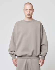 A person with a shaved head models the LIVE FAST DIE YOUNG Basic Blank Sweater in an oversize fit, light gray Baumwolle-Polyester blend, paired with matching pants, standing facing forward against a plain white background. | model