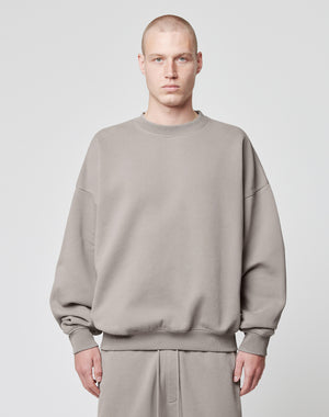 A person with a shaved head models the LIVE FAST DIE YOUNG Basic Blank Sweater in an oversize fit, light gray Baumwolle-Polyester blend, paired with matching pants, standing facing forward against a plain white background.