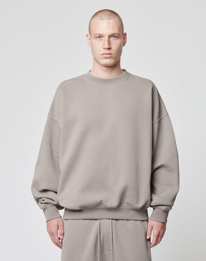 A person with a shaved head models the LIVE FAST DIE YOUNG Basic Blank Sweater in an oversize fit, light gray Baumwolle-Polyester blend, paired with matching pants, standing facing forward against a plain white background. | model