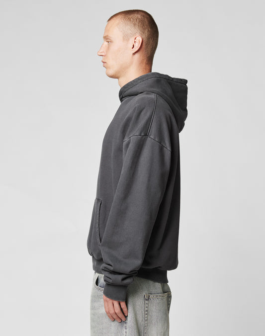 A person with short hair, wearing an Oversize Fit LFDY Core Hooded sweatshirt by LIVE FAST DIE YOUNG in dark gray and light-wash jeans, stands in profile against a plain light gray background.