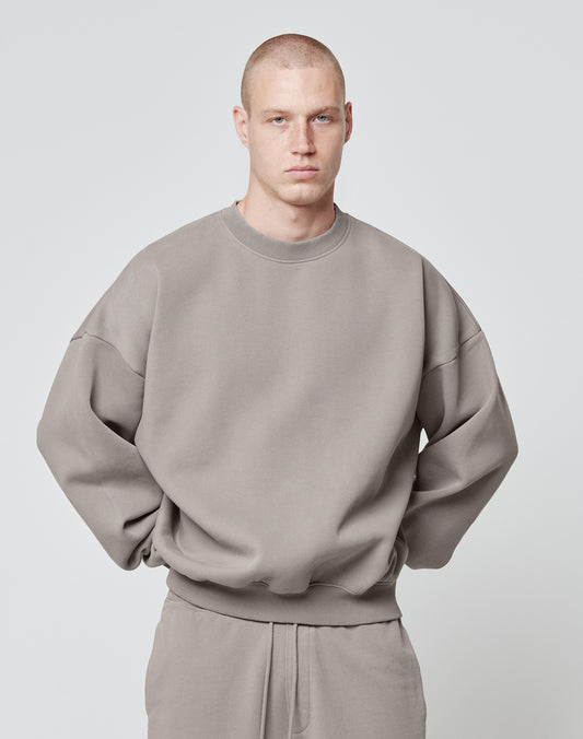 A person with a shaved head wears the LIVE FAST DIE YOUNG Basic Blank Sweater and matching pants, both in beige cotton-polyester vintage wash, standing facing forward against a plain light background with hands behind their back.