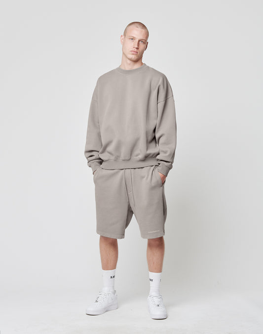 A person stands against a plain white background, wearing a grey LIVE FAST DIE YOUNG Basic Blank Sweater and matching shorts in soft cotton-polyester. White crew socks and sneakers complete the look, hands in pockets, expression neutral.