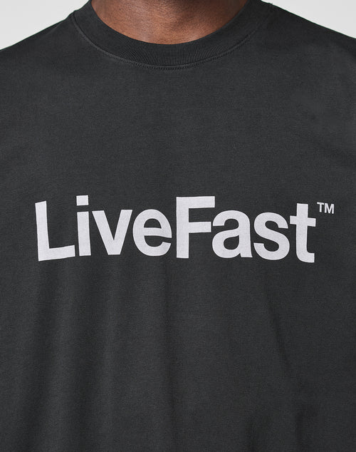 A person wears the Basic LiveFast Tee by LIVE FAST DIE YOUNG, a black regular-fit cotton T-shirt with a bold LiveFast™ front print in large white letters across the chest.