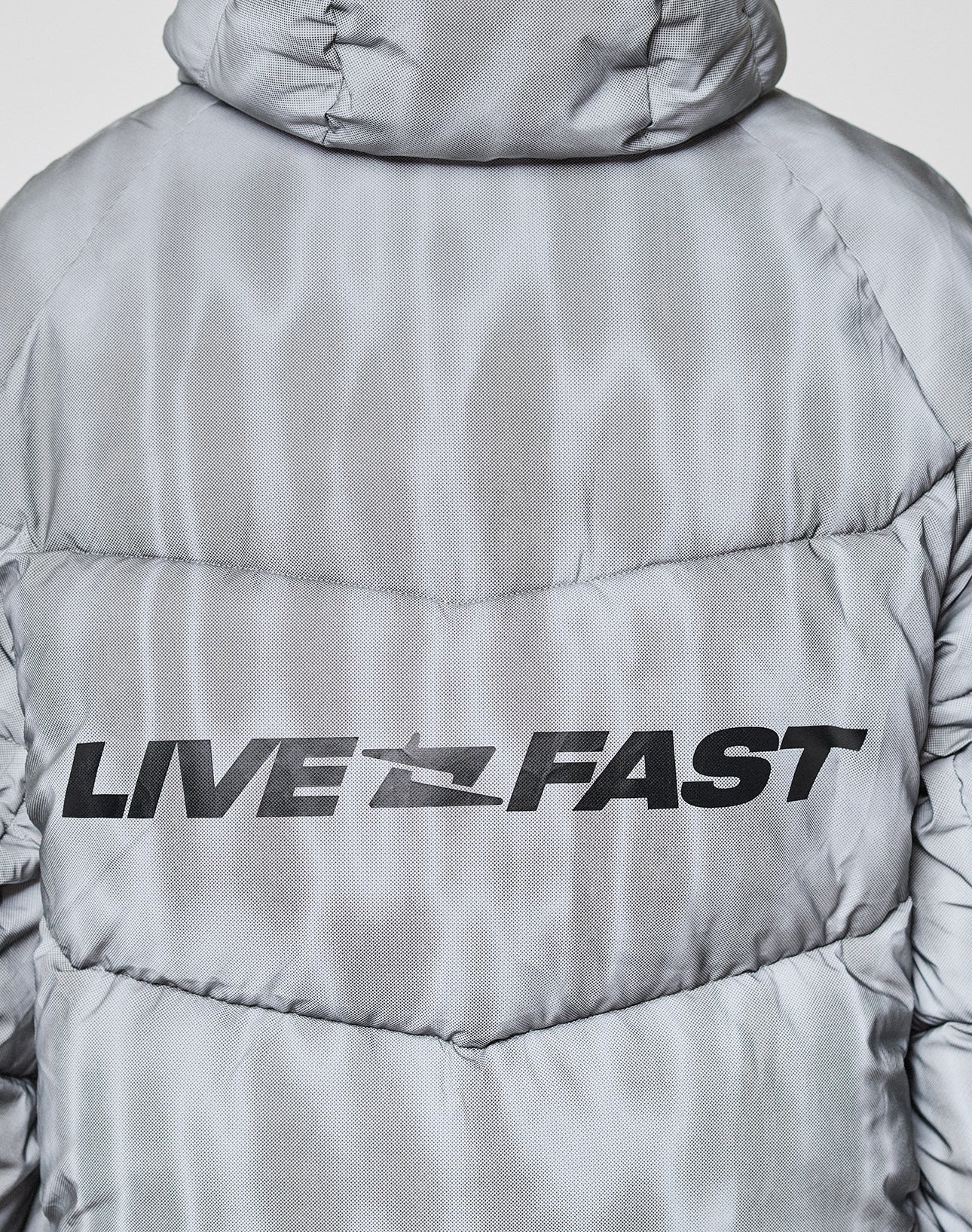 A close-up of the back of the silver-gray, oversize Live Fast Puffer Jacket by LIVE FAST DIE YOUNG, featuring "LIVE FAST" printed in bold black letters.