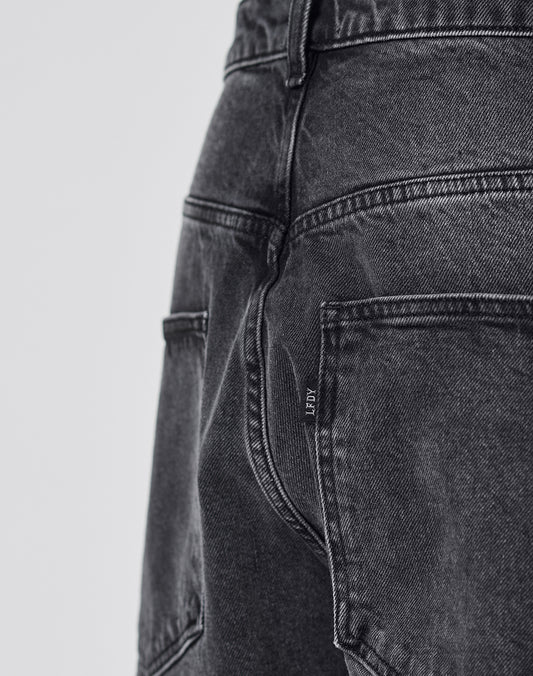 Close-up of the back of a person wearing LIVE FAST DIE YOUNG LFDY Tire Tracks Denim in a Baggy Fit, featuring faded black denim, visible seams, stitching, back pockets, and a small fabric tag on one pocket.