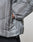 A close-up of a hand in the side pocket of the light gray, textured Live Fast Puffer Jacket by LIVE FAST DIE YOUNG, featuring a visible zipper and elastic cuff, paired with dark pants.