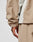 A close-up of a hand and arm wearing the LIVE FAST DIE YOUNG Basic Shell Jacket in an oversize fit light beige and off-white, with matching beige pants, highlighting the cuff, side details, and water-repellent zipper.