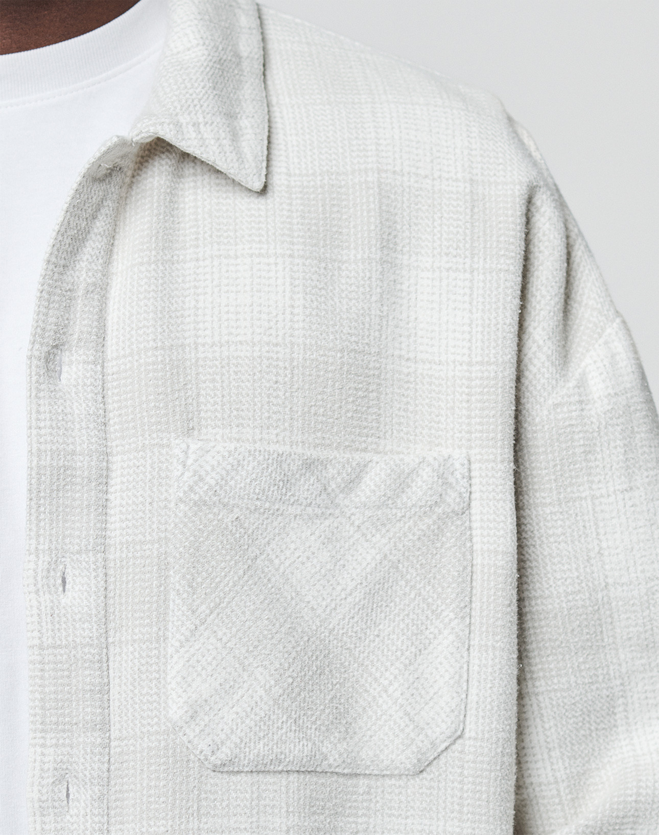 Close-up of a person wearing the LIVE FAST DIE YOUNG Vintage Flannel in an oversized fit over a white T-shirt. The image highlights the textured, light plaid pattern, chest pocket, fabric detail, and relaxed style.