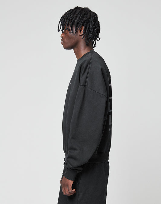 A person with short, twisted hair stands in profile facing left, wearing the LIVE FAST DIE YOUNG Basic Evidence Sweater and matching black Baumwolle Polyester pants against a plain light gray background.