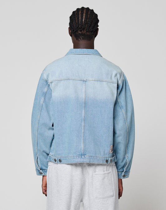 A person with braided hair is shown from behind, wearing a light blue LFDY Trucker Jacket by LIVE FAST DIE YOUNG and light gray shorts, standing against a plain light gray background.