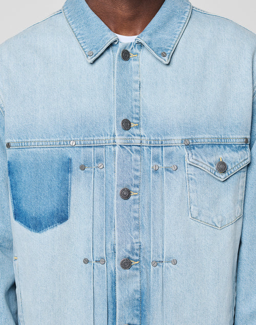 Close-up of the LFDY Trucker Jacket by LIVE FAST DIE YOUNG in light blue denim, Regular Fit, featuring metal buttons and two chest pockets—one with flap, one open. Only the jacket and part of the wearer’s neck are visible.