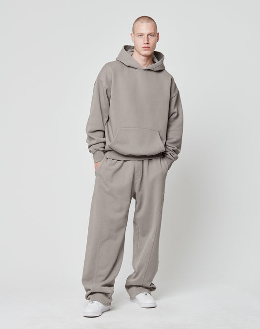 A person wearing the LIVE FAST DIE YOUNG Basic Blank Hooded in an oversize fit with matching gray Baumwolle-Polyester pants and white sneakers stands with hands in pockets against a plain light background, expression neutral.