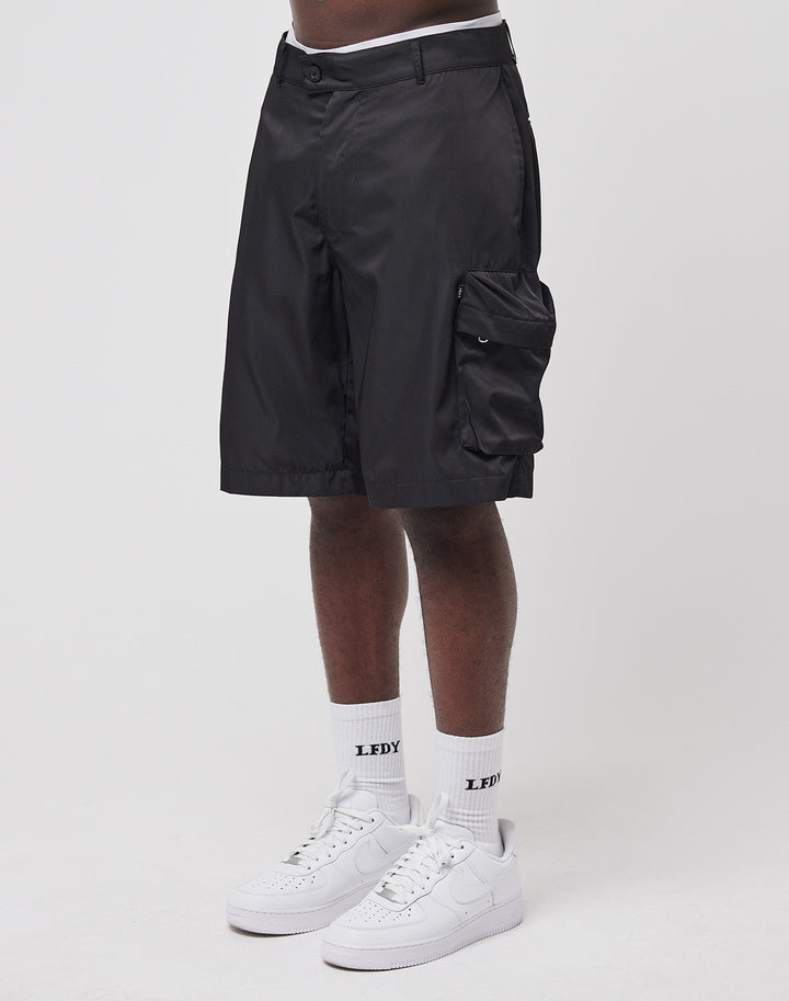A person wearing black LIVE FAST DIE YOUNG Nylon Cargo Shorts, white socks with “LFDY” text, and white Nike sneakers stands against a plain white background. | model