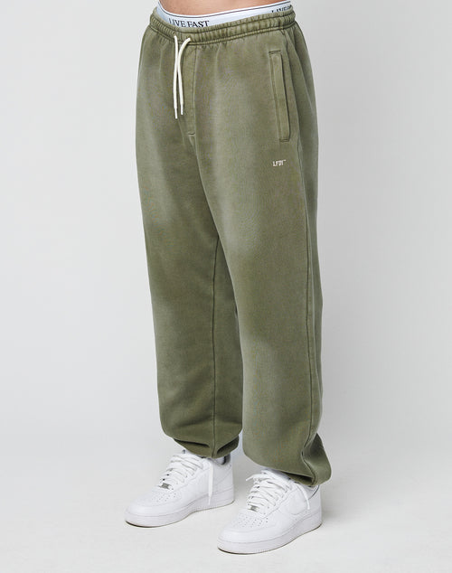 A person wearing olive green Basic Loose Jogger sweatpants by LIVE FAST DIE YOUNG with side pockets, white sneakers, and an elastic waistband with white drawstrings. The visible underwear features a bold “LIVE FAST” logo print.