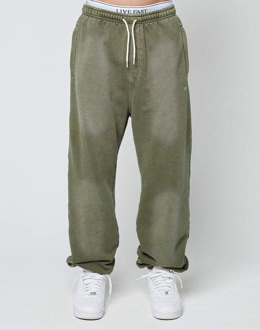 A person wearing LIVE FAST DIE YOUNGās Basic Loose Jogger in olive green with a visible logo waistband and white sneakers stands against a plain light background.