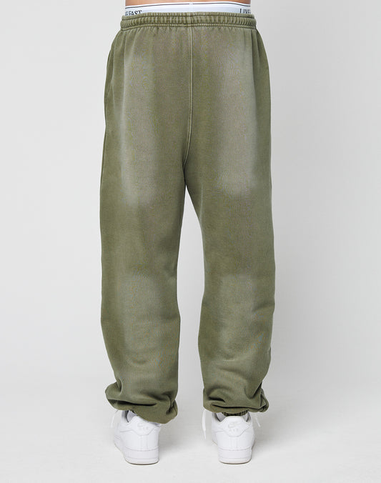 A person is shown from the back wearing LIVE FAST DIE YOUNG Basic Loose Jogger in olive green with a subtle logo print, relaxed fit, and elastic waistband, paired with white sneakers against a plain white background.