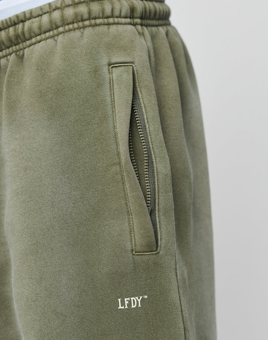 Close-up of LIVE FAST DIE YOUNGs Basic Loose Jogger in olive green, featuring a relaxed fit, zipper pocket, soft fabric with white LFDY⢠embroidery near the pocket, visible stitching on the elastic waistband, and subtle logo print details.
