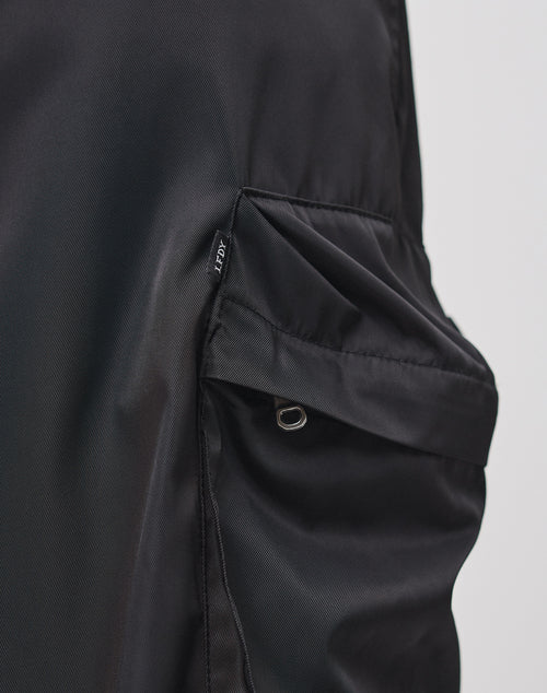 Close-up of LIVE FAST DIE YOUNG Nylon Cargo Shorts in black, featuring diagonal side pockets with small silver grommets and Cargotaschen detailing. The shorts have a slight sheen, set against a plain light background.