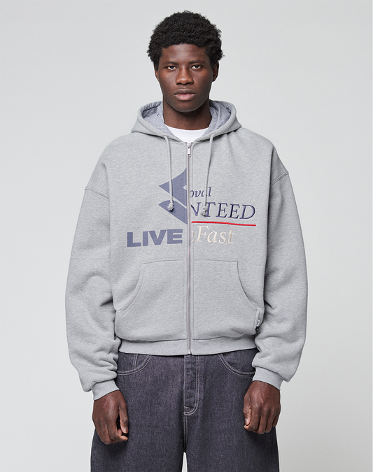 A person wearing a Flannel Lined Hooded Jacket by LIVE FAST DIE YOUNG, featuring a bold graphic and text, pairs it with loose dark gray jeans while standing against a plain light gray background.