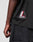 Close-up of a person's left arm and torso wearing the LFDY Mesh Jersey by LIVE FAST DIE YOUNG, featuring an oversize fit, black mesh fabric, and a striking red, white, and black patch. Styled with black denim shorts for a relaxed, on-trend look.