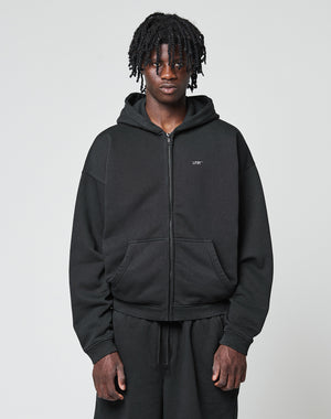 A person with medium-length twists wears a black LIVE FAST DIE YOUNG Basic Hooded Zip and black pants, standing against a plain light gray background, looking directly at the camera with a neutral expression.