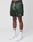 A person wears LIVE FAST DIE YOUNG Basic Satin Shorts in dark green with a white drawstring and elastic waistband, paired with white crew socks featuring green stripes and white sneakers, standing against a plain white background.