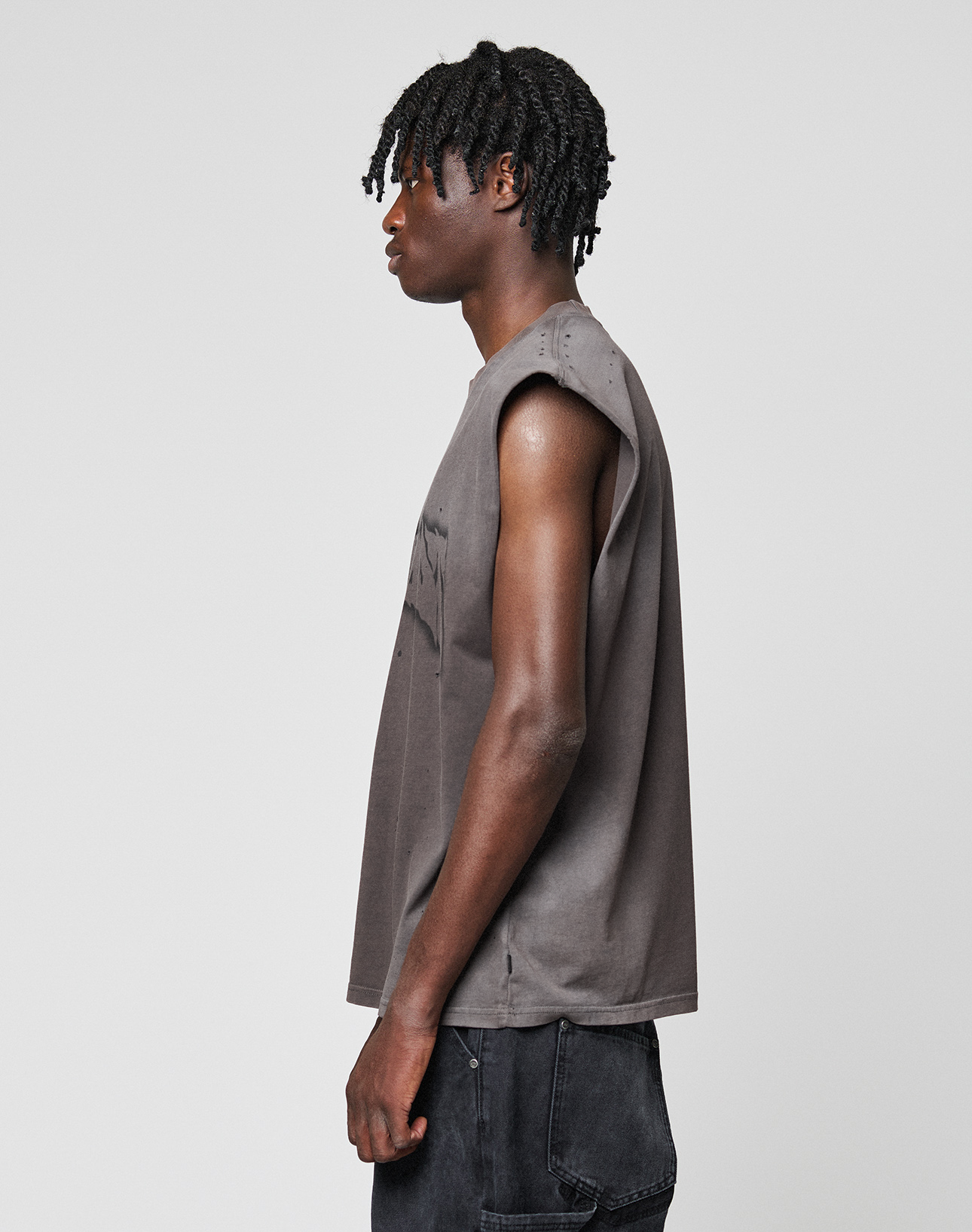 A person with short, twisted hair stands in profile against a plain background, wearing the oversize fit LFDY Flames Muscle Shirt by LIVE FAST DIE YOUNG, made from 100% Baumwolle, paired with dark pants.