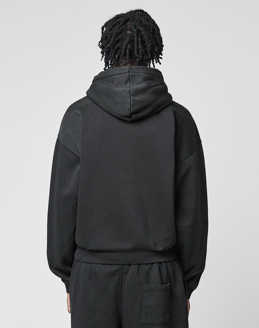 A person with short, twisted hair is seen from behind in a black LIVE FAST DIE YOUNG Basic Hooded Zip and matching black pants, standing against a plain light gray background.