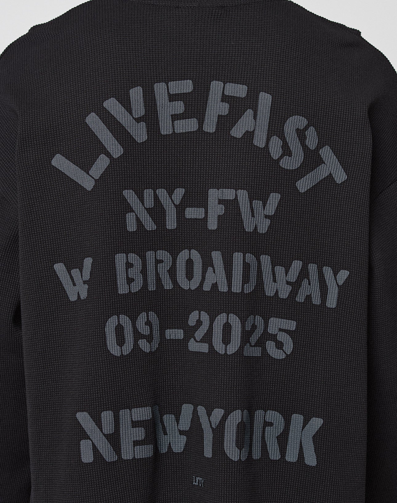 The NY-FW Waffle Longsleeve by LIVE FAST DIE YOUNG features black textured fabric and a bold gray backprint: LIVE FAST NY-FW W BROADWAY 09-2025 NEW YORK, showcased on an oversized fit.