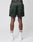 A person faces away, wearing LIVE FAST DIE YOUNG’s Basic Satin Shorts in dark green with an elastic waistband featuring repeated “LFDY” branding. Made from polyester, the shorts are styled with white socks with black stripes and white sneakers.