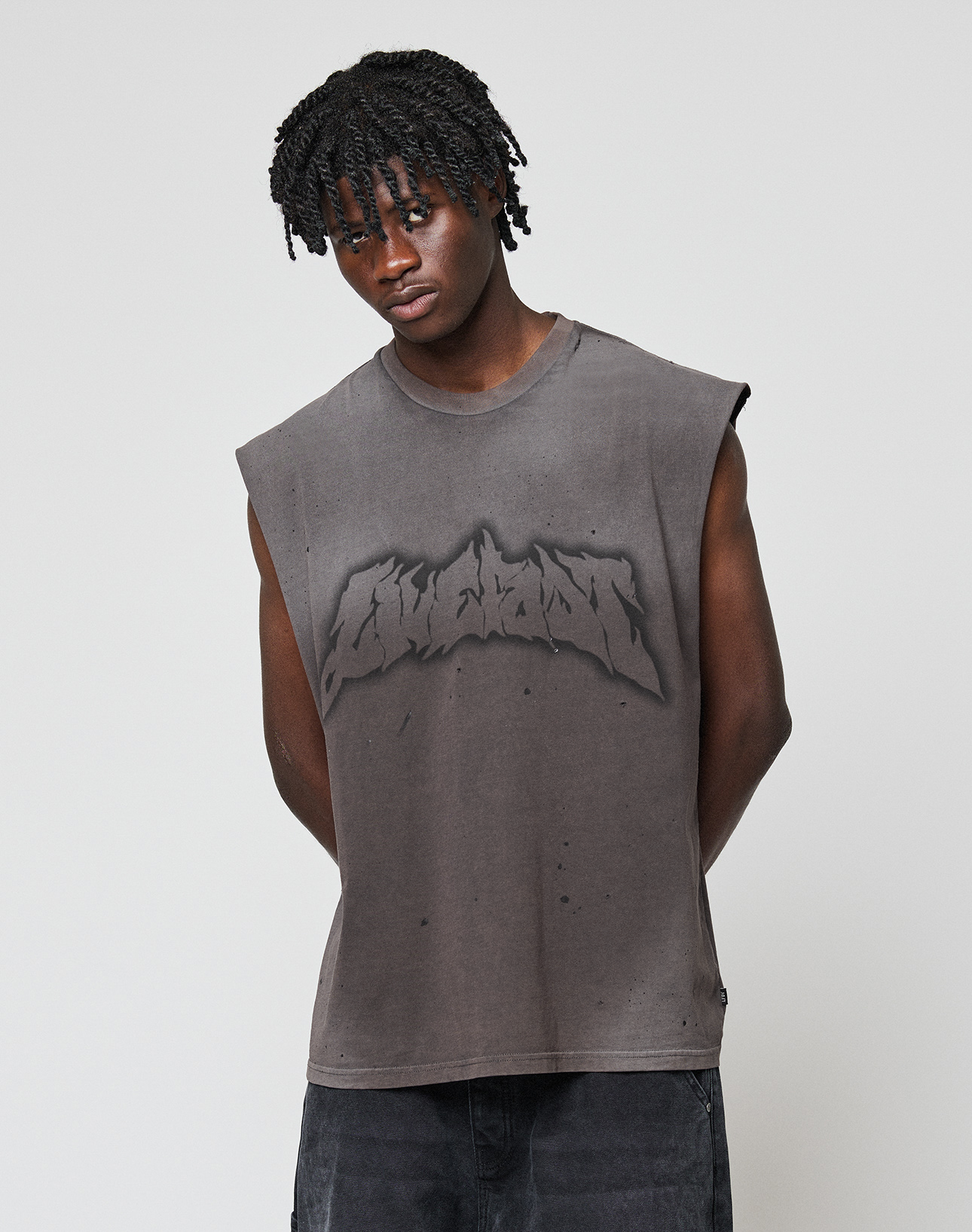 A young man with short, twisted hair wears the LFDY Flames Muscle Shirt by LIVE FAST DIE YOUNG, a sleeveless, faded gray 100% Baumwolle top featuring a bold handgefertigter Sprayeffekt graphic, standing against a plain light gray background.