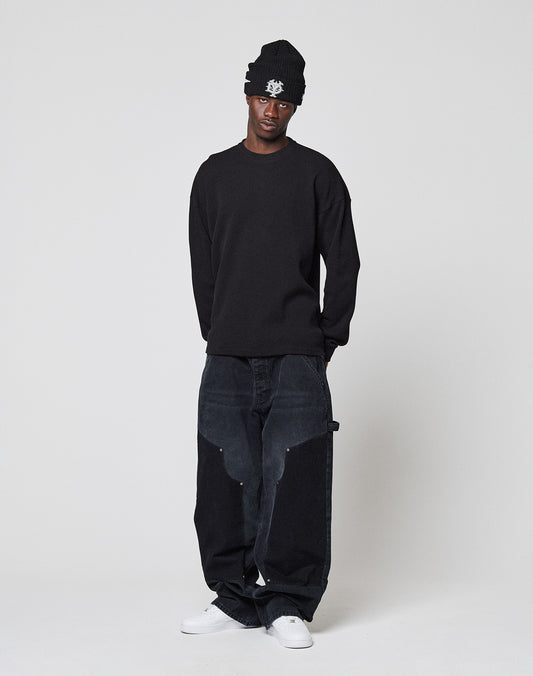 A person stands against a white background, wearing the LIVE FAST DIE YOUNG NY-FW Waffle Longsleeve with backprint, loose faded black jeans, black beanie, and white sneakers. The look is oversize for a modern vibe.