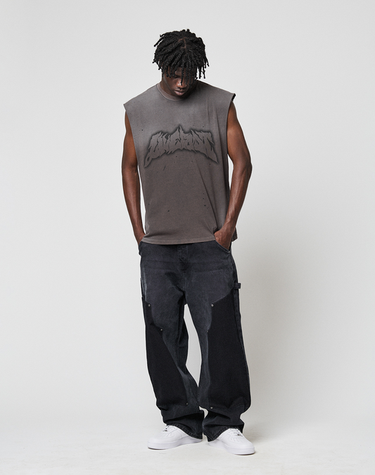 A man with short dreadlocks wears a LIVE FAST DIE YOUNG LFDY Flames Muscle Shirt in faded gray, loose black jeans, and white sneakers, standing against a plain white background with his head slightly bowed and hands in his pockets.