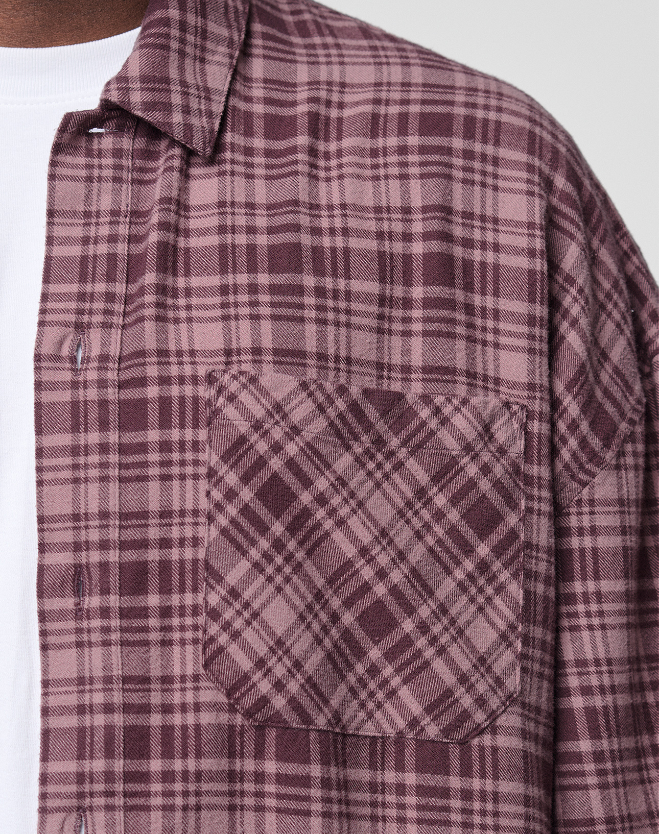 Close-up of a person wearing the LFDY Light Flannel by LIVE FAST DIE YOUNG in maroon and pink plaid over a white tee. The image showcases the chest pocket, LFDY branding, and upper torso; made from 100% Baumwolle. Face not shown.
