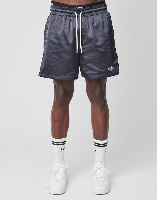 Wearing LIVE FAST DIE YOUNG Basic Satin Shorts in dark gray, paired with white crew socks featuring black stripes and white sneakers, a person stands against a plain light background. Only the lower half of their regular fit is visible.