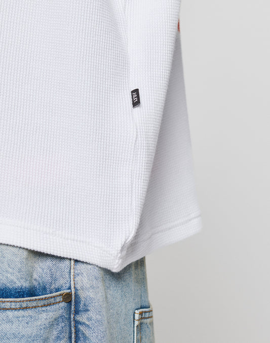 Close-up of the lower part of a LIVE FAST DIE YOUNG NY-FW Waffle Longsleeve in white 100% Baumwolle with a small black tag, styled over light blue faded jeans against a plain, neutral background.