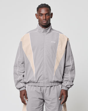 A man stands facing forward in a LIVE FAST DIE YOUNG Basic Nylon Trackjacket, regular fit, light gray and beige with white piping, made from nylon-lycra fabric, against a plain light gray background.