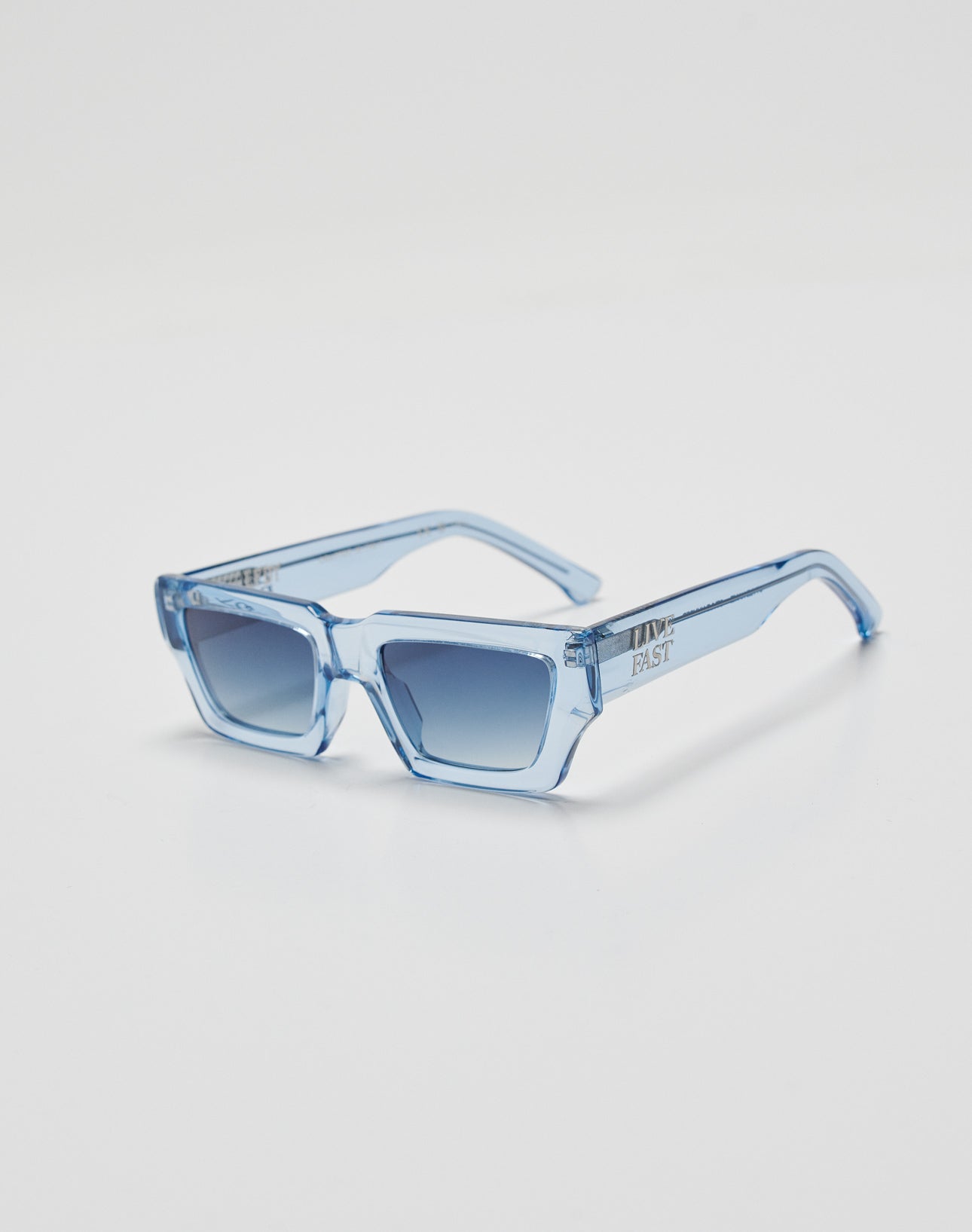 LIVE FAST DIE YOUNG’s Live Fast Sunglasses feature translucent light blue rectangular frames in premium Mazzuchelli Acetat and gradient blue UV-protective lenses, shown on a white background.