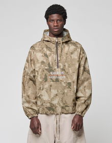 A man with short curly hair wears a LIVE FAST DIE YOUNG LFDY Camo Halfzip Jacket in oversize fit with "CALL US 449Livefast" on the front, paired with light beige 100% Baumwolle pants, standing against a light gray backdrop.