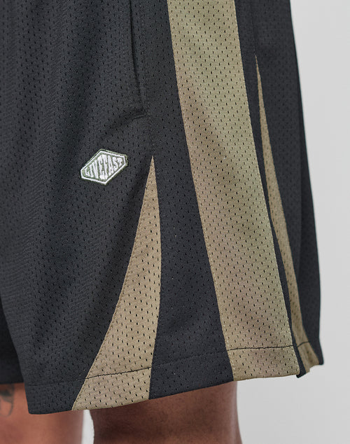 Close-up of a person wearing LIVE FAST DIE YOUNG Striped Mesh Shorts in black with olive green stripes and logo patch, crafted from breathable polyester mesh.