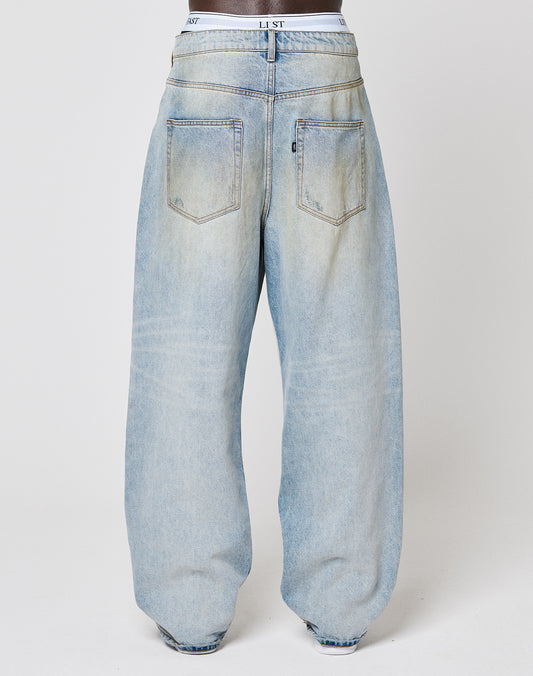 Back view of a person in LIVE FAST DIE YOUNG’s LFDY Baggy Denim, light-wash blue jeans with two back pockets and a white waistband, standing against a plain white background.