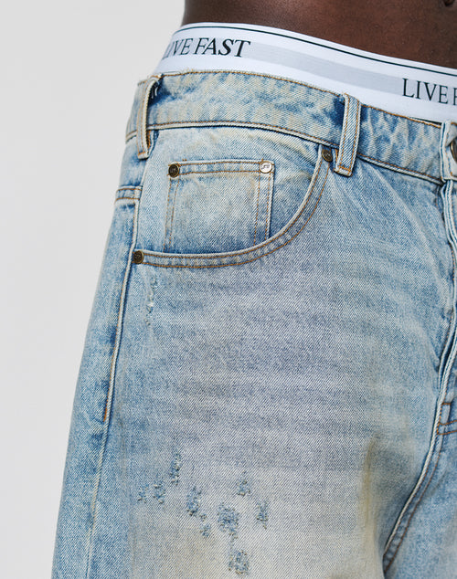 Close-up of a person in LFDY Baggy Dirt Denim jeans by LIVE FAST DIE YOUNG, light blue and slightly distressed with a straight leg. Made from 100% Baumwolle, paired with white underwear featuring a LIVE FAST waistband.