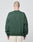 A person with a shaved head stands with their back to the camera, wearing the LIVE FAST DIE YOUNG Basic Chest Sweater in dark green (oversize fit) and light beige shorts, against a plain light gray background.