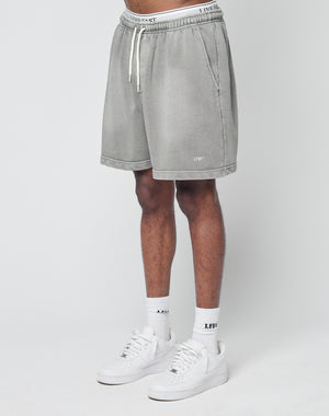 A person wearing LIVE FAST DIE YOUNGs Basic Sweat Shorts in light gray, LFDY logo white socks, and white sneakers stands against a plain white background, with only their lower half visible.