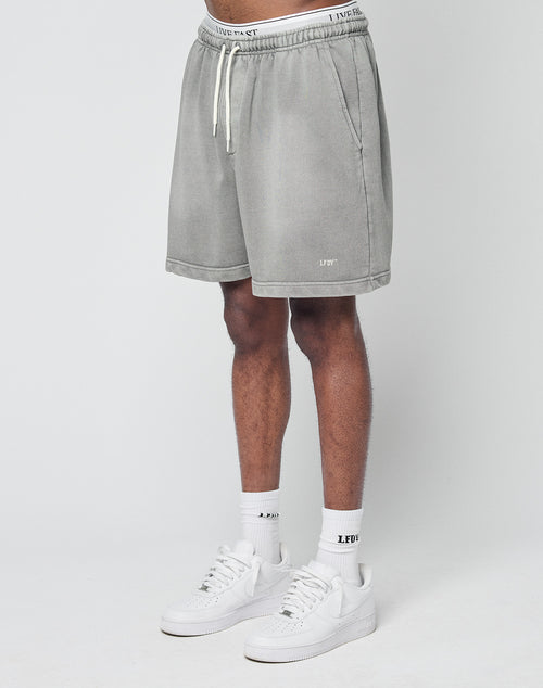 A person wearing LIVE FAST DIE YOUNGs Basic Sweat Shorts in light gray, LFDY logo white socks, and white sneakers stands against a plain white background, with only their lower half visible.