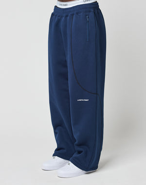 A person wears the LFDY Active Fleece Jogger by LIVE FAST DIE YOUNG in wide fit navy with black piping, LIVE FAST logo on waistband and thigh, Reißverschluss Taschen, and white sneakers. The background is plain white.